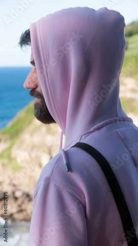 Hombre barbudo con sudadera de algodón rosa frente al mar photo