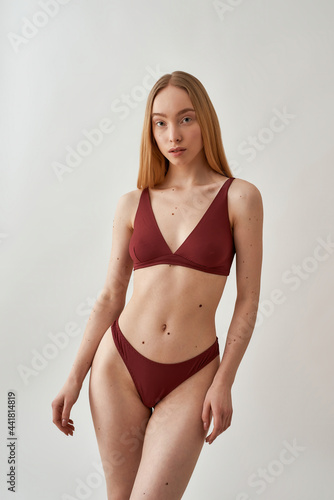 Attractive young slim caucasian woman with beautiful perfect body wearing burgundy underwear posing isolated over light gray background