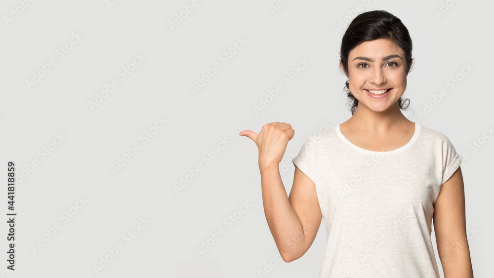 Portrait of smiling Indian woman isolated on grey studio background point at blank empty copy space. Happy millennial mixed race female show good promotion deal or sale discount. Commerce concept. - obrazy, fototapety, plakaty 