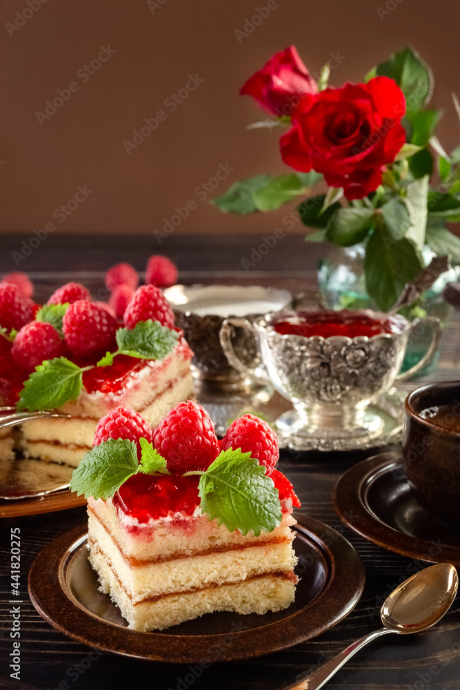 Cake. A piece of beautiful raspberry cake on a plate. Raspberry jam in a silver bowl. Festive food. Bouquet of red roses in a vase. Postcard. Poster. High quality photo