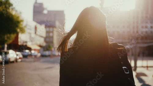Following young tourist beautiful woman wearing black business jacket and bag, enjoying sunlight in big city, walking down the street. photo