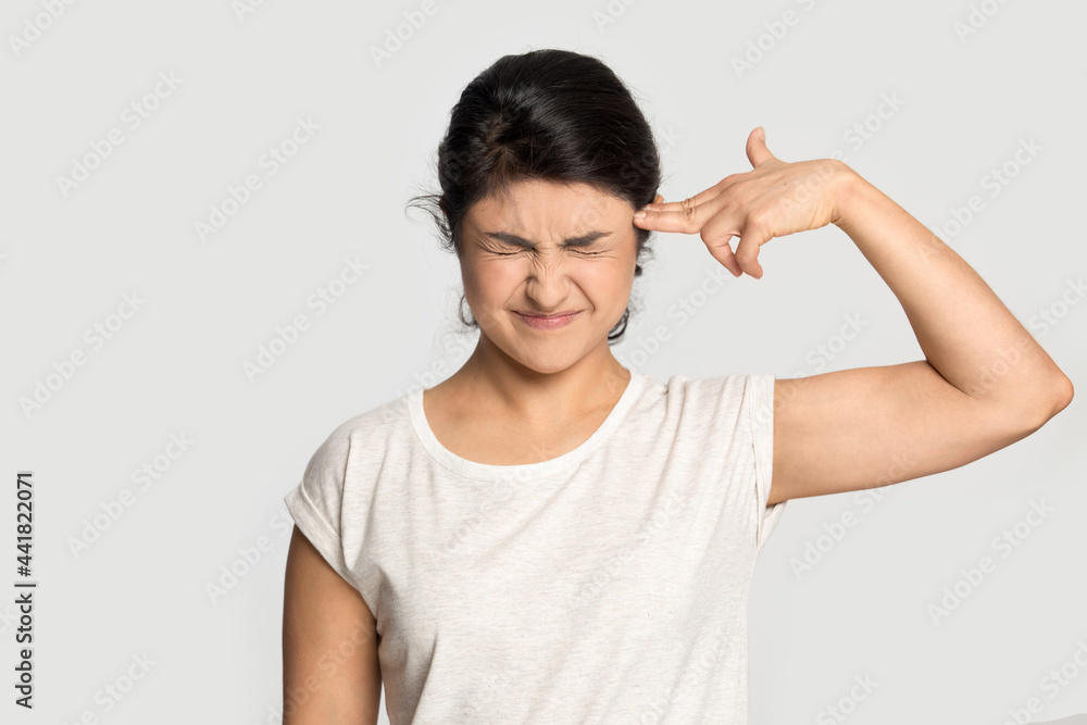 Unhappy young Indian woman isolated on grey studio background feel depressed put imaginary gun shoot kill herself. Upset mixed race female suffer from problems have anxiety. Depression concept. Unhappy young Indian woman isolated on grey studio background feel depressed put imaginary gun shoot kill herself. Upset mixed race female suffer from problems have anxiety. Depression concept.