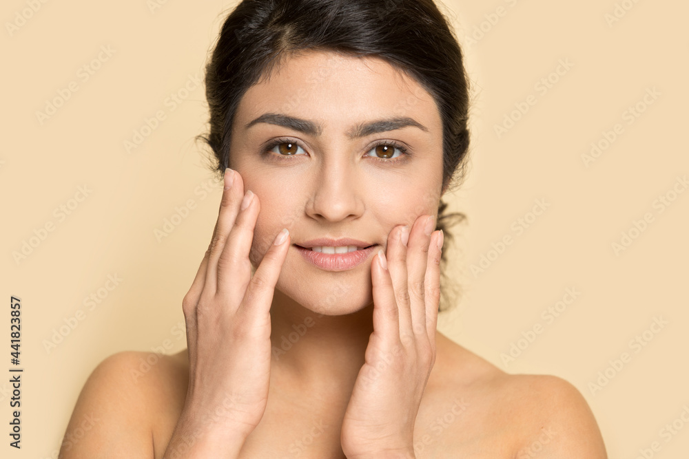 Portrait of young Indian woman isolated on yellow studio background touch healthy face skin after beauty salon procedures. Smiling mixed race female satisfied with facial treatment. Skincare concept. Portrait of young Indian woman isolated on yellow studio background touch healthy face skin after beauty salon procedures. Smiling mixed race female satisfied with facial treatment. Skincare concept.