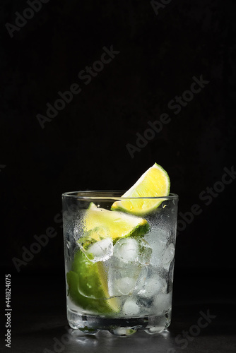 Glass of lime lemonade on a dark table, summertime drinks. Homemade lemonade with lime and ice cube. Idea cold fresh drinks