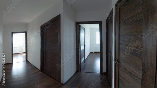 Panoramic photo of the apartment corridor with white walls  dark wooden doors and dark laminate flooring.