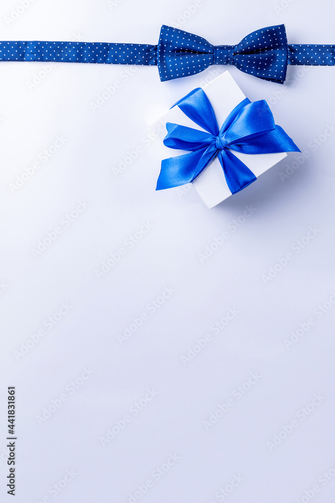Father day gift. White box with bow ribbon, blue bowtie or tie on light background. Concept of Fathers Day greeting card, copy space for text.