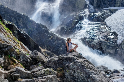 Beautiful blonde tourist is sitting on a rock above the Siklawa waterfall in the Polish Tatra Mountains.