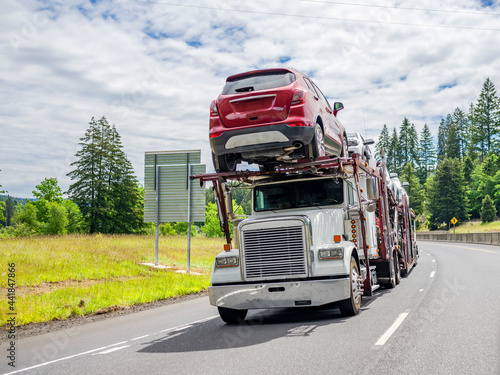 Capacious car hauler big rig semi truck transporting cargo on modular semi trailer driving on the summer highway road