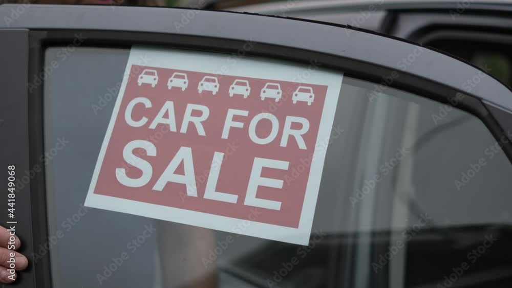 A man is placing a car for sale sign in the window of his car waiting for somebody to by his vehicle A man is placing a car for sale sign in the window of his car waiting for somebody to by his vehicle