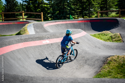 A young child rides the new South Glenmore Park BMX pump track on his bike on a summer evening in Calgary Alberta Canada.