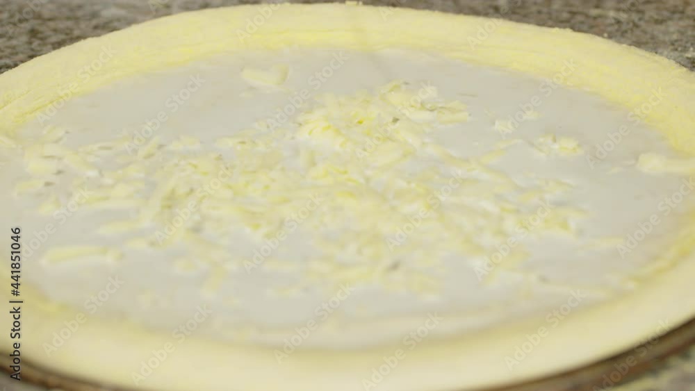 Sprinkling fresh grated cheese on pizza dough, close up. Chef is cooking pizza. Process of preparing traditional italian pizza.