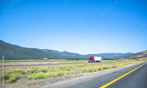 Long haul industrial freight big rig red semi truck with semi trailer transporting goods driving on the flat road in California