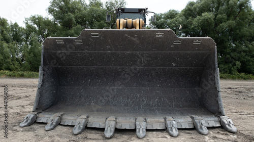 Quarry wheel loader shovel with big metal teeth seen in Longmont, Colorado, USA, on a sandy ground with green trees in the background
