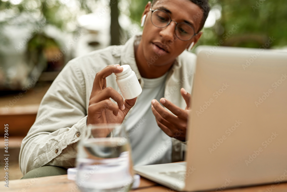Man showing pills container into laptop screen Man showing pills container into laptop screen