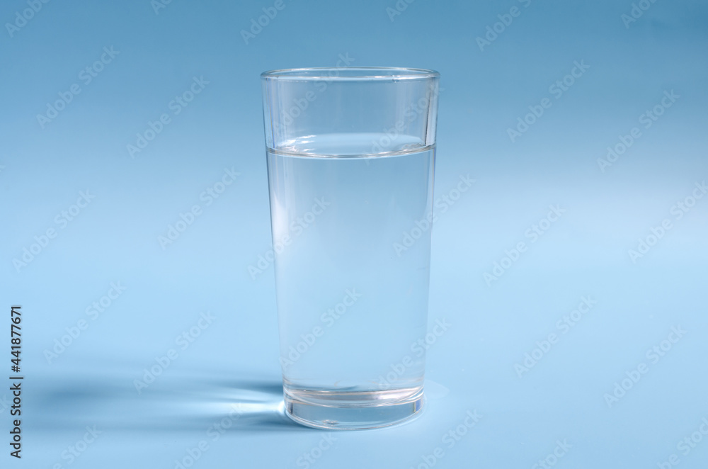 A glass of clear water on a blue background close-up. A glass of water on a colored background A glass of clear water on a blue background close-up. A glass of water on a colored background