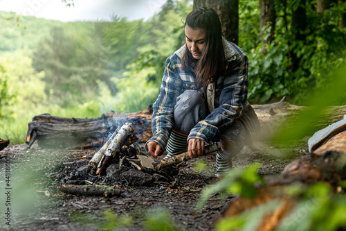 A girl on a hike in the woods prepares a fire.