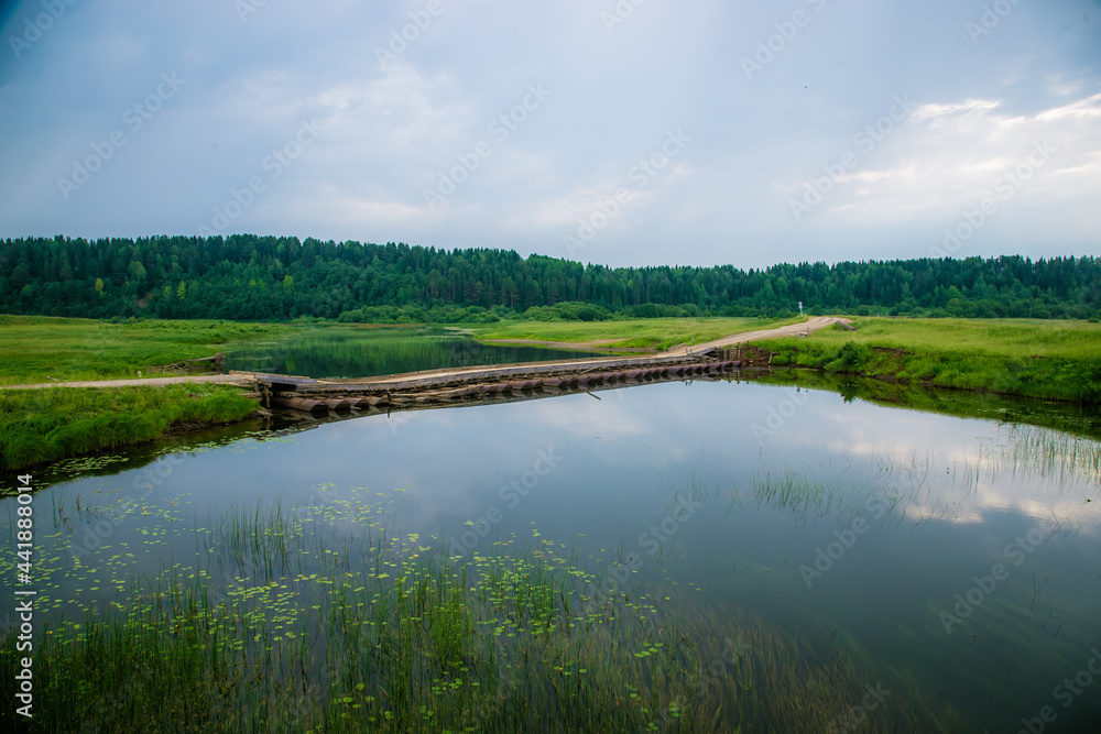 a dirt road goes over a pontoon bridge over a small river