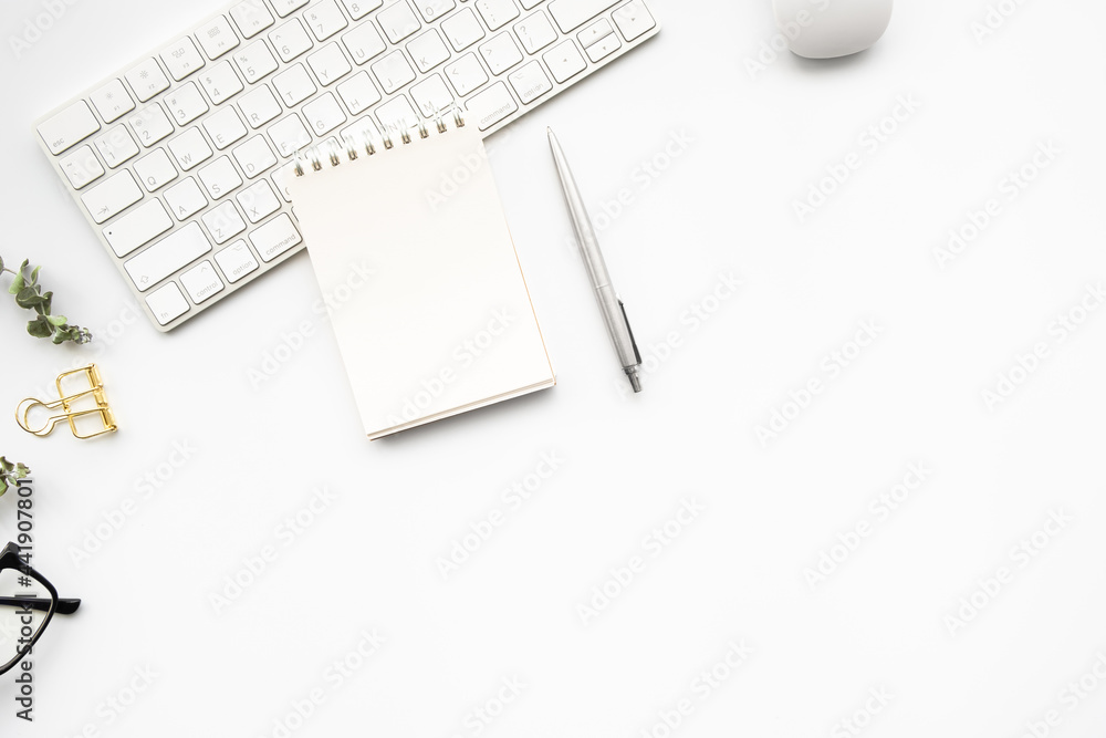 Small blank notebook with pen are on top of computer keyboard over white woman office desk table with office supplies. Top view with copy space, flat lay. Small blank notebook with pen are on top of computer keyboard over white woman office desk table with office supplies. Top view with copy space, flat lay.