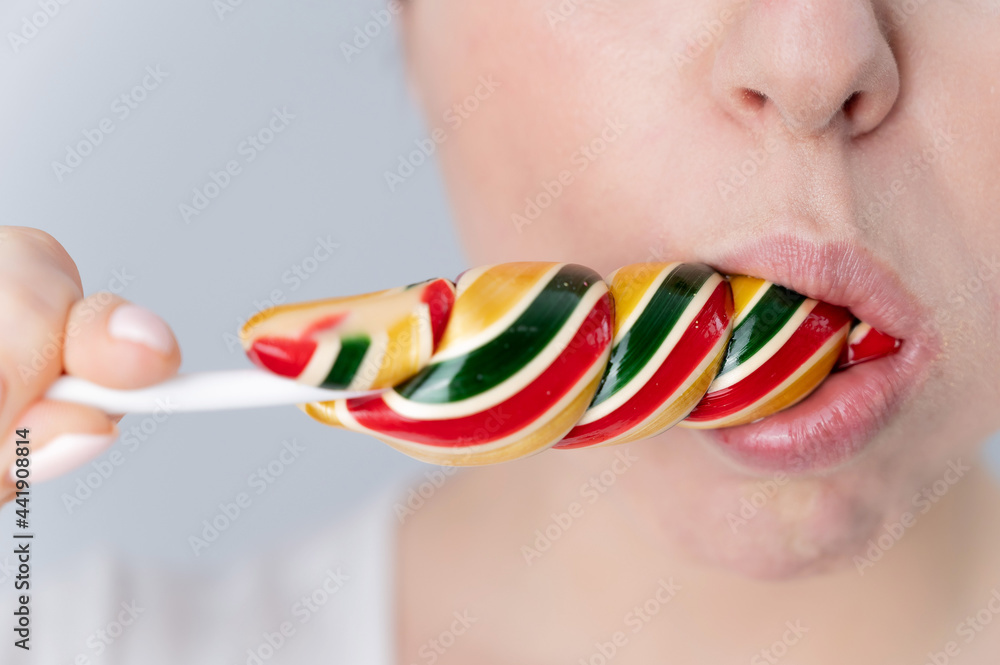 Naklejka premium Close-up portrait of a woman sucking a long lollipop against a white background. Blowjob simulation
