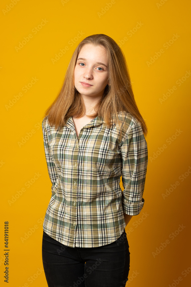 Beautiful teenager girl, with a cute smile, in jeans and a plaid shirt, posing on a yellow background. Beautiful teenager girl, with a cute smile, in jeans and a plaid shirt, posing on a yellow background.