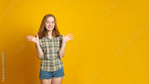 Banner copy space. Optimistic girl raises palms from joy, happy to receive awesome present from someone, dressed in casual shirt, isolated on yellow background. Excited female happy.