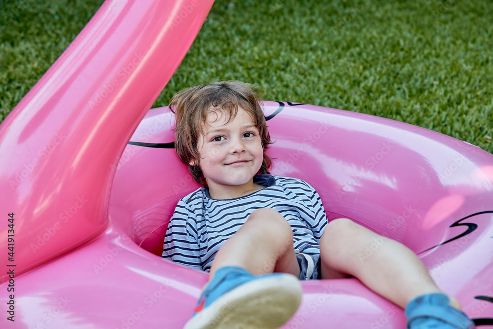 Playful kid lying on inflatable pink flamingo on lawn Playful kid lying on inflatable pink flamingo on lawn