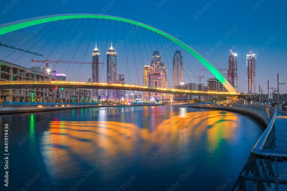Fototapeta premium Illuminated in green color Tolerance Bridge in Dubai with an unusual architectural design against the backdrop of skyscrapers. Urbanism and sightseeing in the UAE