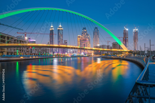 Illuminated in green color Tolerance Bridge in Dubai with an unusual architectural design against the backdrop of skyscrapers. Urbanism and sightseeing in the UAE