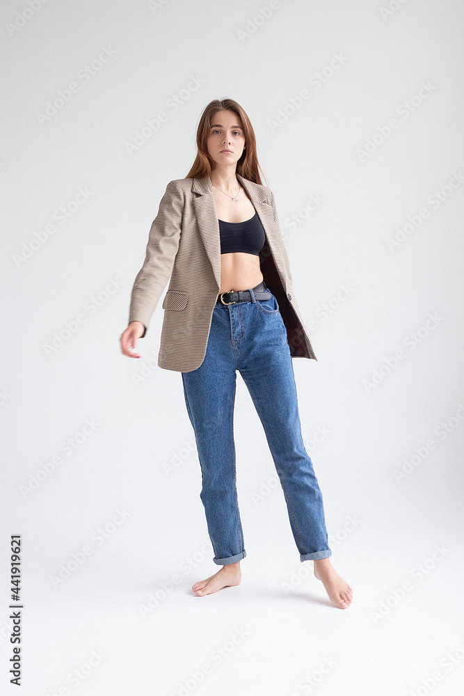 portrait of young caucasian attractive woman with long brown hair in blue jeans, black top and suit jacket on white background. skinny pretty lady posing at studio with bare feet portrait of young caucasian attractive woman with long brown hair in blue jeans, black top and suit jacket on white background. skinny pretty lady posing at studio with bare feet
