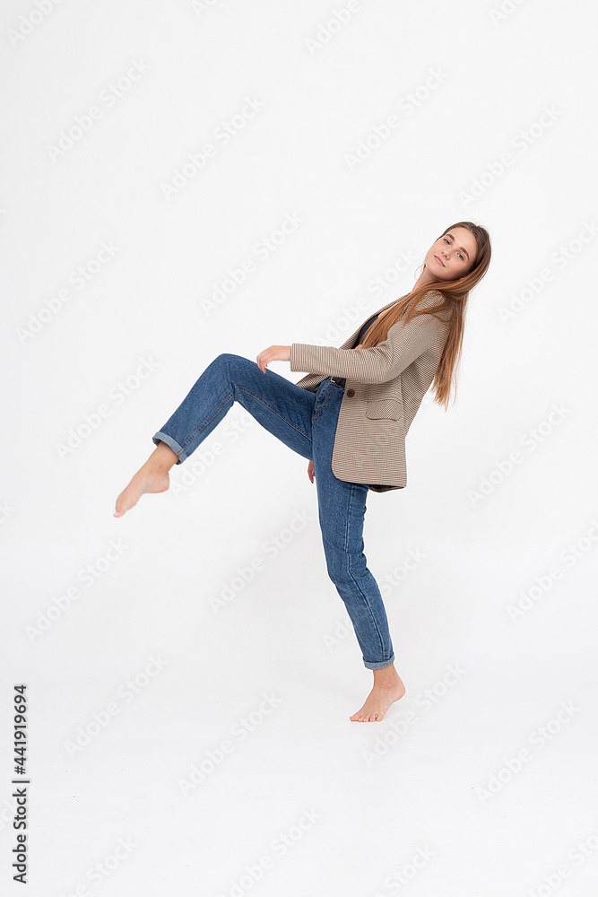 portrait of young caucasian attractive woman with long brown hair in blue jeans and suit jacket on white background. skinny pretty lady posing at studio with bare feet
