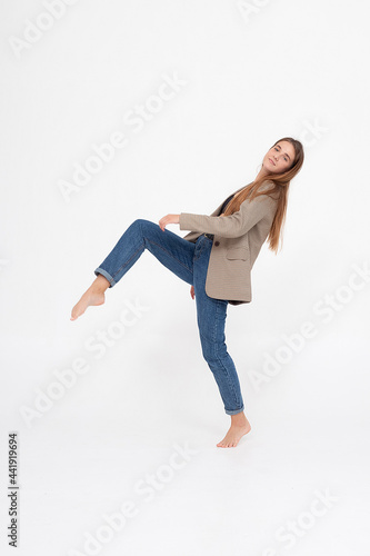 portrait of young caucasian attractive woman with long brown hair in blue jeans and suit jacket on white background. skinny pretty lady posing at studio with bare feet