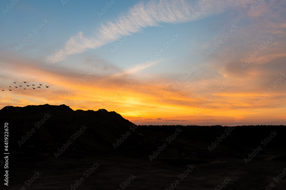 Sand mountain peaks and June evening sunset. Orange sky, clouds.