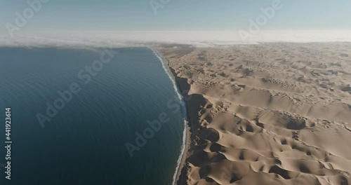 Aerial close-up panning view where the endless sand dunes meet the coastline of the Atlantic Ocean in the Namib desert