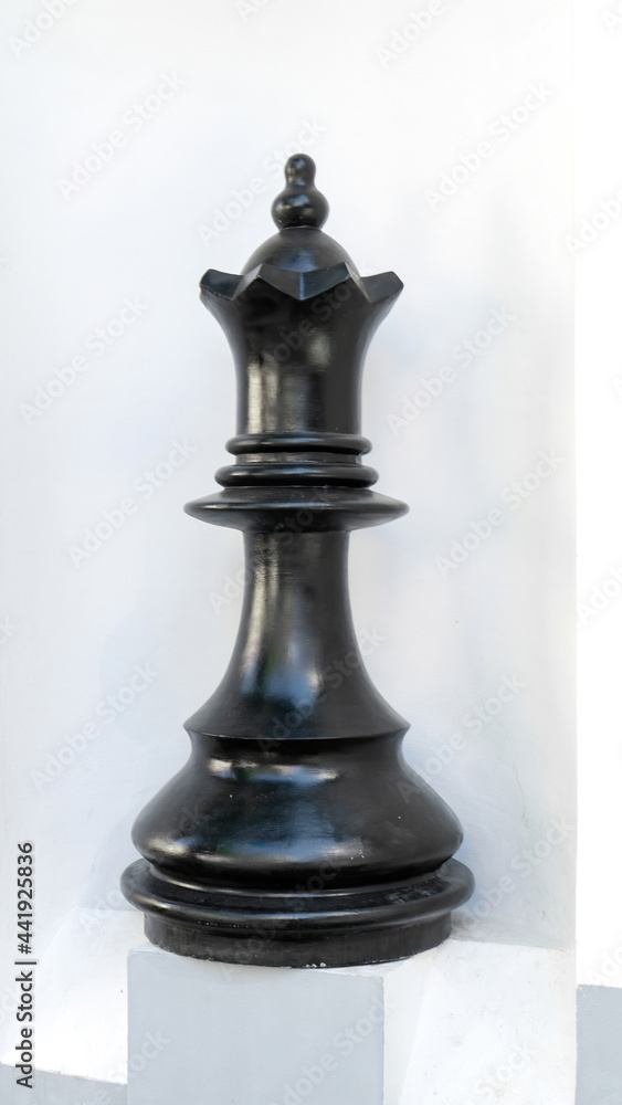 A huge chess piece of the black queen on a pedestal in the park. Black chess piece of the queen on a white background.