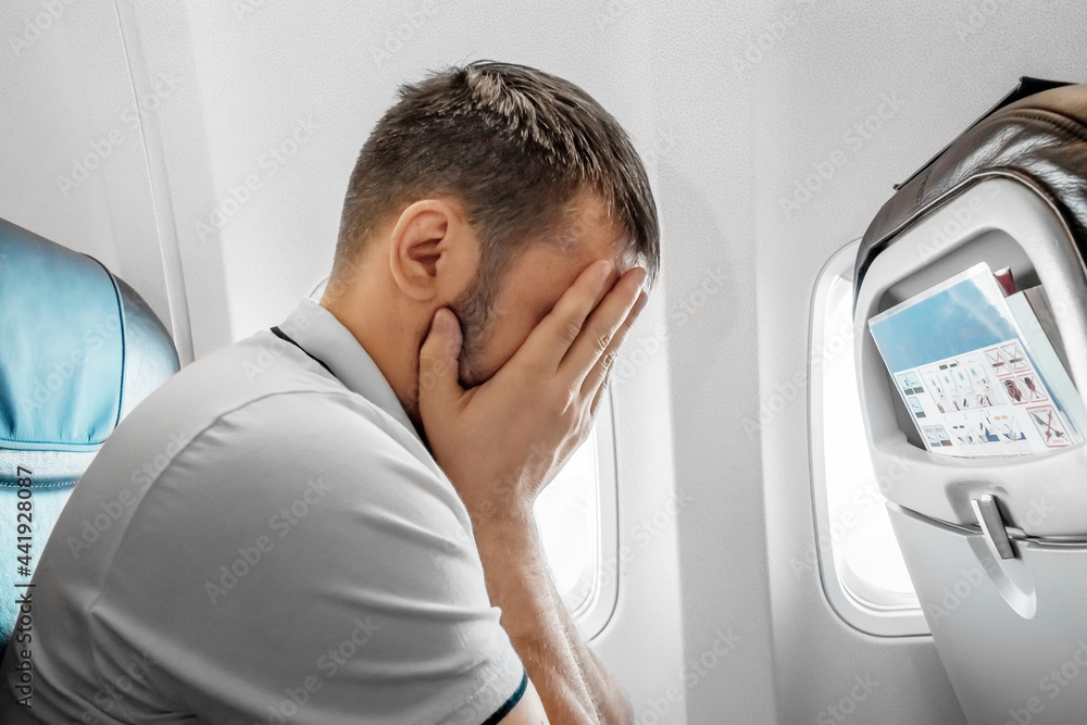 A man sits in front of an airplane window and is nervous, afraid to fly, the cabin of a passenger aircraft. Aerophobia, fobilya, international flights. A man sits in front of an airplane window and is nervous, afraid to fly, the cabin of a passenger aircraft. Aerophobia, fobilya, international flights.