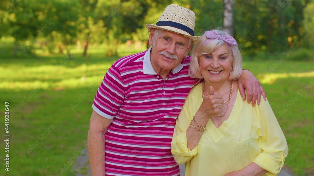 Portrait of senior old stylish tourists man and woman walking in summer park and embracing. Elderly grandmother grandfather enjoying date, traveling together. Active mature family after retirement