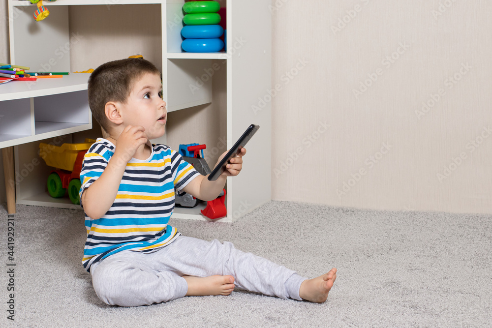 A small child 3-4 years old and a mobile phone in the children's room with room for text to copy the space. Cartoons and dependence on gadgets in children, limiting children from adult content on the A small child 3-4 years old and a mobile phone in the children's room with room for text to copy the space. Cartoons and dependence on gadgets in children, limiting children from adult content on the