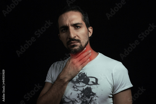 Sore throat. A man holding on to a sore throat on a black background.