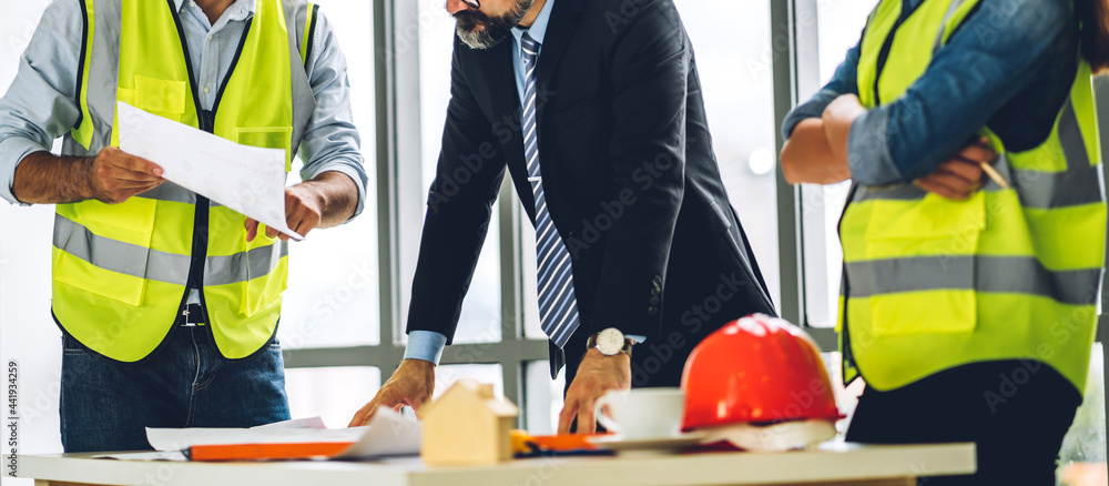 Professional of team engineer cargo foreman in helmets working with blueprint and construction tool on table at the construction site Professional of team engineer cargo foreman in helmets working with blueprint and construction tool on table at the construction site