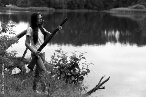Beautiful woman with vintage shotgun near the lake in black and white