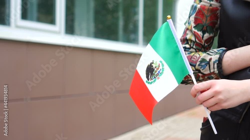 Unrecognizable woman holding Mexican flag. Girl walking down street with national flag of Mexico