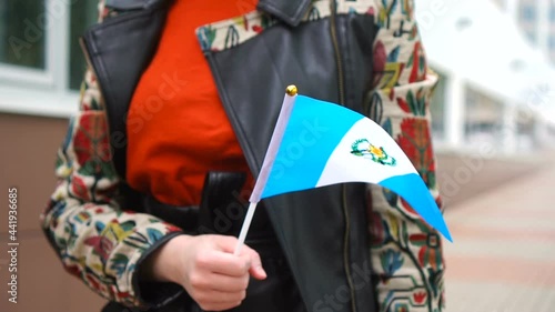 Unrecognizable woman holding Guatemalan flag. Girl walking down street with national flag of Guatemala