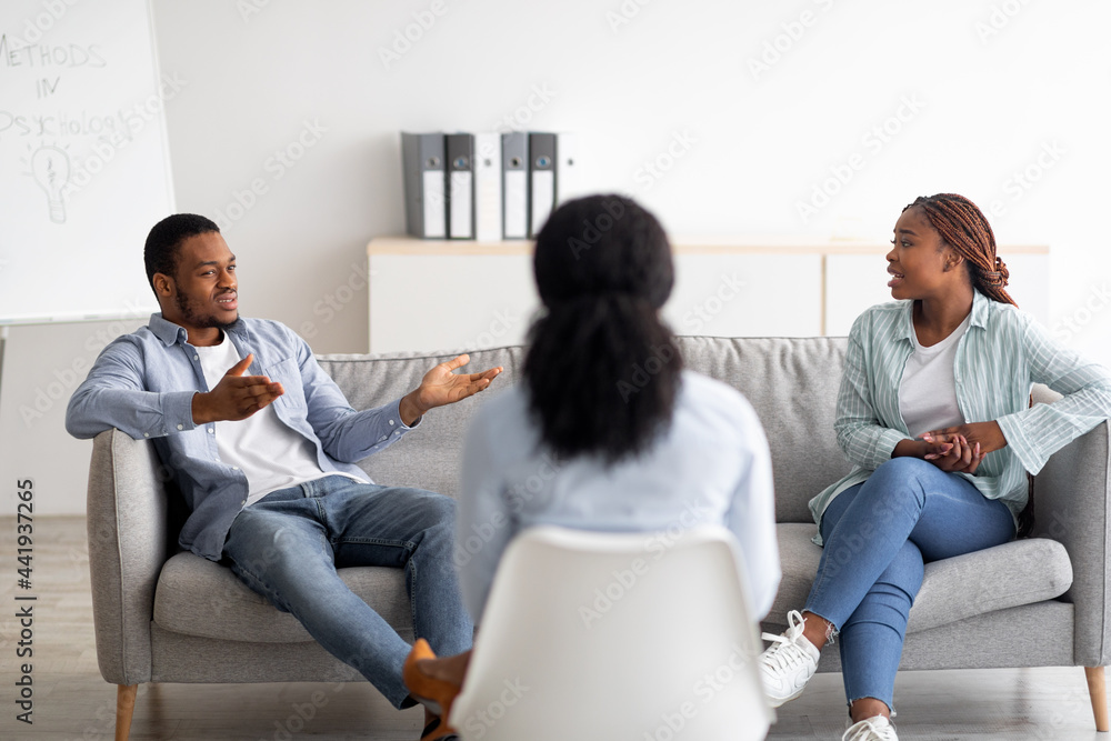 Female psychotherapist sitting with her back to camera during session with irritated black couple at clinic Female psychotherapist sitting with her back to camera during session with irritated black couple at clinic