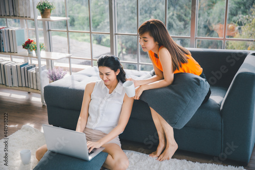Two Asian females sitting on couch writing working with computer laptop at home office, Mobile working concept