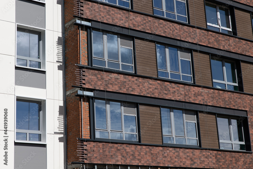 The facade of a residential building against a background of blue sky and greenery. Construction concept.
The facade of a residential building against a background of blue sky and greenery. Construction concept.