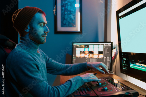 Attractive Male Video Editor Works with Footage or Video on His Personal Computer, he Works in Creative Office Studio or home. Neon lights photo