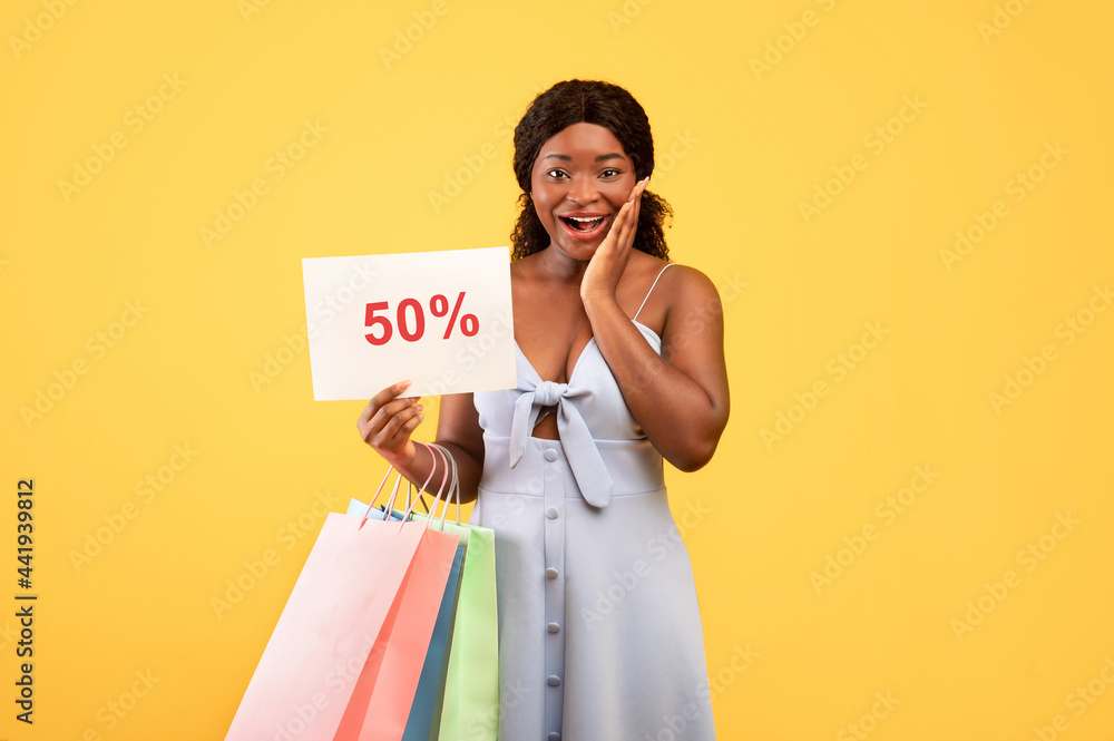 Huge summer sales. Excited young African American woman holding shopping bags and FIFTY PERCENT OFF sign Huge summer sales. Excited young African American woman holding shopping bags and FIFTY PERCENT OFF sign
