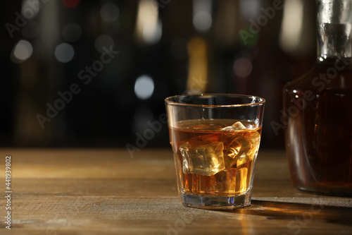 Glass of whiskey with ice on wooden table in bar  space for text