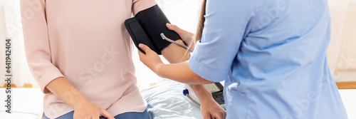 Young woman having her blood pressure checked by a nurse, doctor or a health visitor. Heart health banner. Blood pressure digital gauge monitor. © andreaobzerova