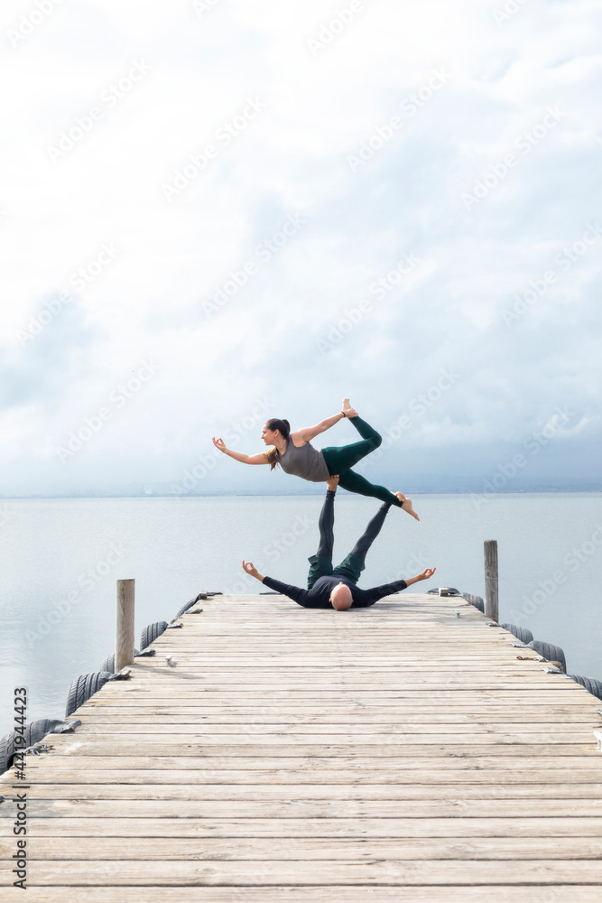 Couple practicing acroyoga on a dock on a lake Couple practicing acroyoga on a dock on a lake
